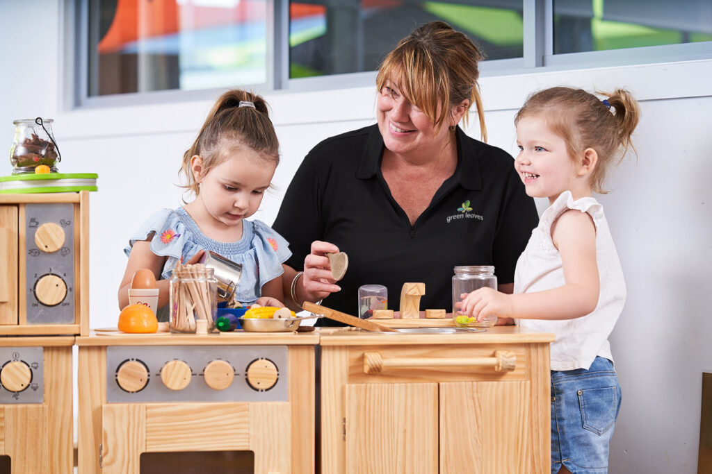 green leaves educator playing with 3 year olds in garden at childcare